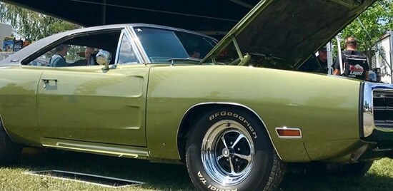 A classic car with its hood up in front of a Meguiar's tent.
