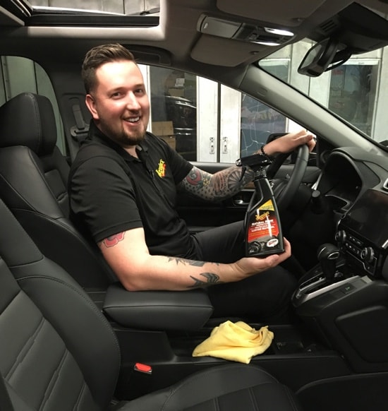 Owner of Showcar Detailing Canada, Joel Prior, sitting in the driver seat of a car and holding a bottle of Meguiar's® Natural Shine Protectant.