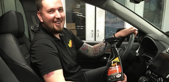 Owner of Showcar Detailing Canada, Joel Prior, sitting in the driver seat of a car and holding a bottle of Meguiar's® Natural Shine Protectant.

