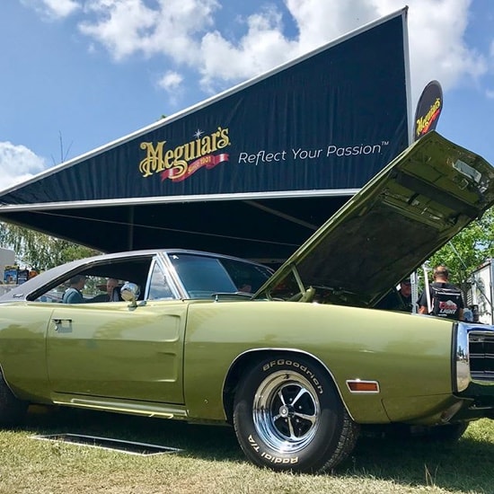 Une voiture classique avec son capot levé, devant une tente Meguiar’s.